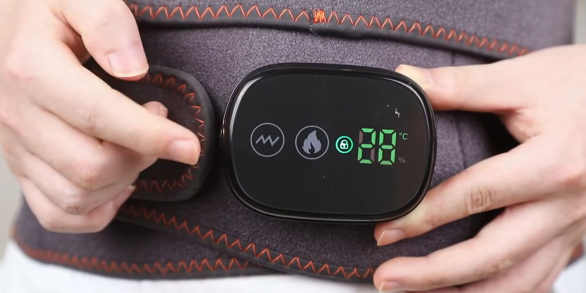 Deux mains posées sur le boîtier de commande de la ceinture Dorséa portée à la taille : la touche massage, la touche chaleur, le cadenas de verrouillage et l'afficheur indiquant la température en degrés